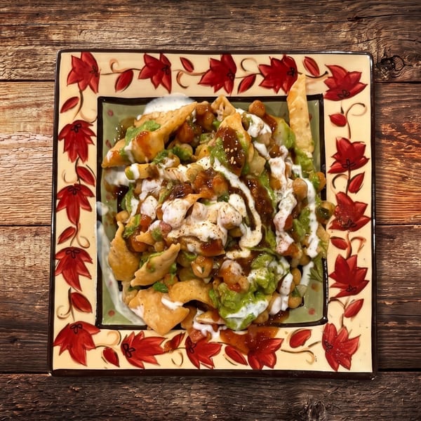 A colorful plate of Indian chaat, topped with chickpeas, sauces, and crispy fried dough.